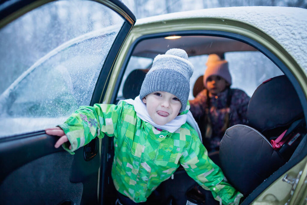 Boy looks out of a car door during a family road trip to the winter forest. Active weekend - Photo, Image