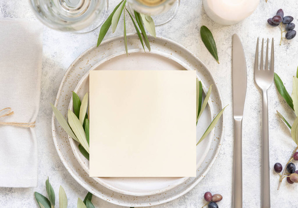 Davetiye kartı ve zeytin dallarıyla süslenmiş porselen tabaklar olan düğün masası. Kare boş kağıt kartın düz olduğu zarif modern şablon. Akdeniz modeli, boşluğu kopyala - Fotoğraf, Görsel
