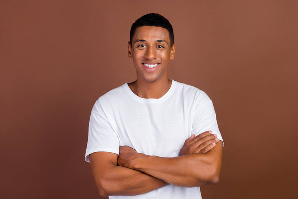 Fénykép szép fiatal brunet srác keresztbe karok viselnek fehér póló elszigetelt barna színű háttér - Fotó, kép