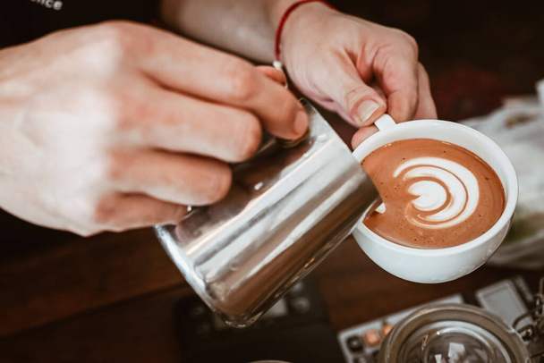 Barista gieten gestoomde melk om hete koffie aan het maken van latte kunst. Een latte is een koffie drankje gemaakt met espresso en gestoomde melk. - Foto, afbeelding