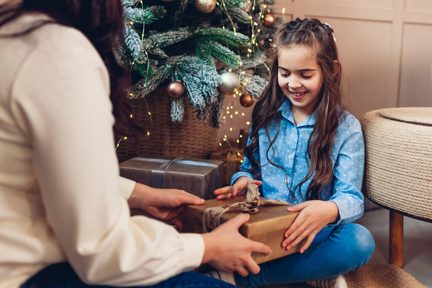 Boldog karácsonyt és boldog új évet! Anya és lánya ajándékot cserélnek otthon a fa alatt. A család jól érzi magát. - Fotó, kép