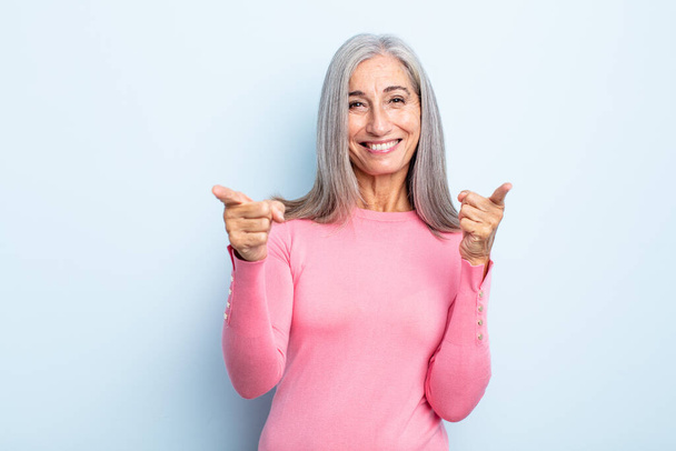 middle age gray hair woman smiling with a positive, successful, happy attitude pointing to the camera, making gun sign with hands - Foto, Bild