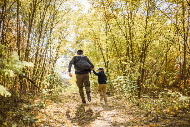 Vader en zoon brengen tijd door in het bos. Gelukkige vader en kindje genieten van de herfstvakantie in een zonnig park. Kinderen houden van ouders affectie en tederheid, mooie familie. - Foto, afbeelding