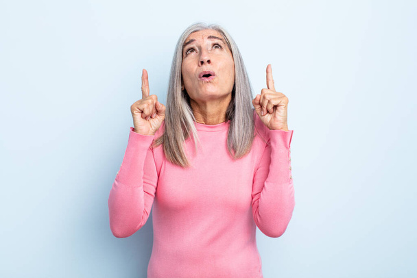 middle age gray hair woman feeling awed and open mouthed pointing upwards with a shocked and surprised look - 写真・画像