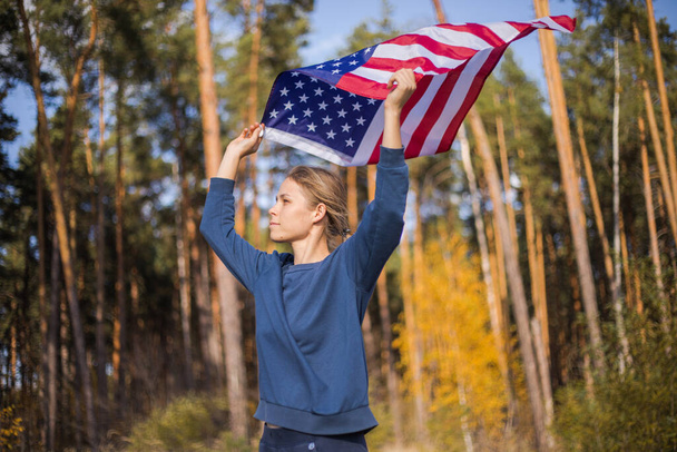 Beautiful girl with American flag. American flag in hands on warm summer forest - Photo, Image