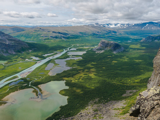 Vue aérienne panoramique depuis le sommet rocheux de Skierffe sur la vallée glaciaire du delta de la rivière Rapadalen au parc national de Sarek avec des méandres, des lacs, des montagnes et des bouleaux. Paysage du jour d'été Suède Laponie - Photo, image
