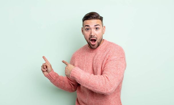 young handsome man feeling shocked and surprised, pointing to copy space on the side with amazed, open-mouthed look - 写真・画像