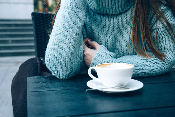 Frau im kuscheligen blauen Pullover trinkt Kaffee in einem Straßencafé - Foto, Bild
