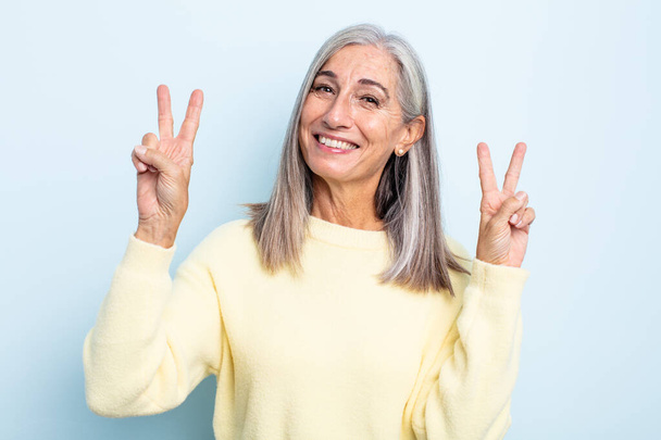 middle age gray hair woman smiling and looking happy, friendly and satisfied, gesturing victory or peace with both hands - Fotó, kép