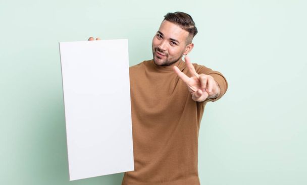 young handsome man smiling and looking happy, gesturing victory or peace. empty canvas concept - Photo, image