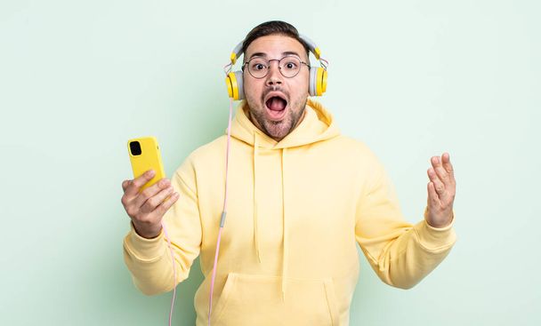 young handsome man feeling extremely shocked and surprised. headphones and smartphone concept - Fotoğraf, Görsel