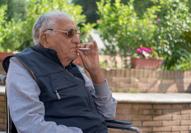 Ο ηλικιωμένος καπνίζει στον κήπο. - Φωτογραφία, εικόνα