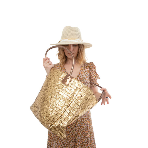 Large female bag of gold color in the hands of a woman in a brown dress isolated on a white background. - Φωτογραφία, εικόνα
