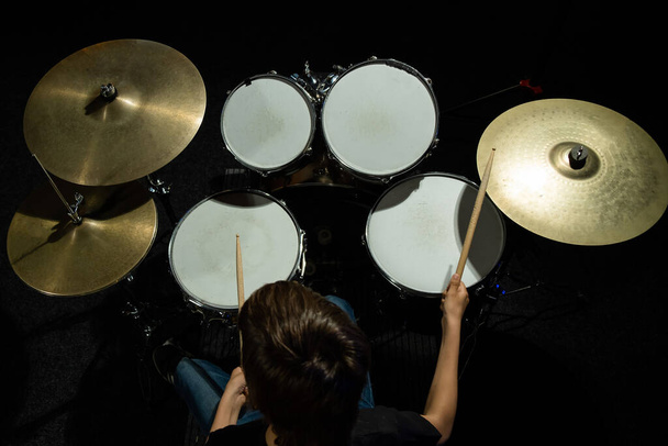 Vista dall'alto di un ragazzo che impara a suonare la batteria in studio su uno sfondo nero. Studente di una scuola di musica. - Foto, immagini