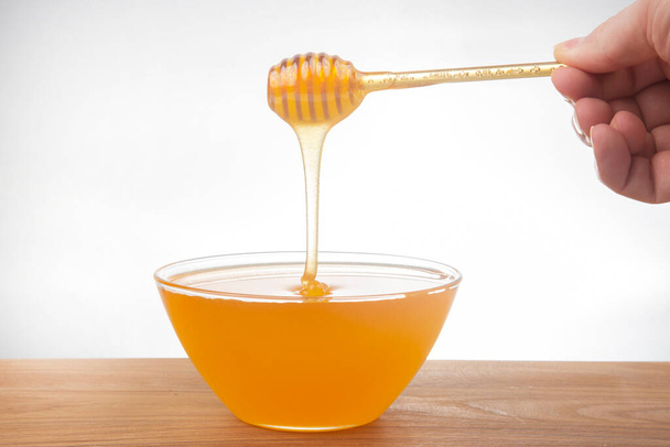 verse honing druipt van een lepel in een transparante plaat op een witte achtergrond. biologische vitamine gezondheidsvoeding - Foto, afbeelding