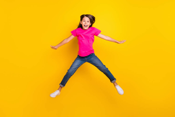 Photo of crazy active cheerful girl jump open mouth wear pink t-shirt jeans sneakers isolated yellow color background - Foto, Imagem