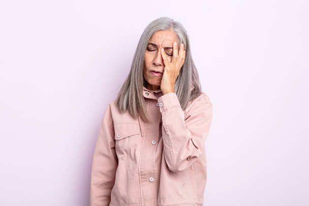 middle age gray hair woman feeling bored, frustrated and sleepy after a tiresome, dull and tedious task, holding face with hand - Foto, Imagen