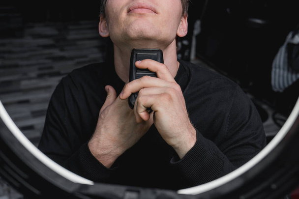 A guy shaves with an automatic razor next to the ring lighting. Care for your appearance. - Foto, imagen