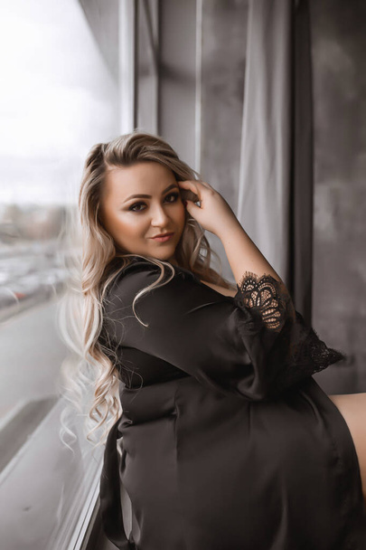 Plus-size woman with long blond hair in lingerie , overweight blonde with lush forms in the loft, full girl in black clothes with bright makeup - Zdjęcie, obraz