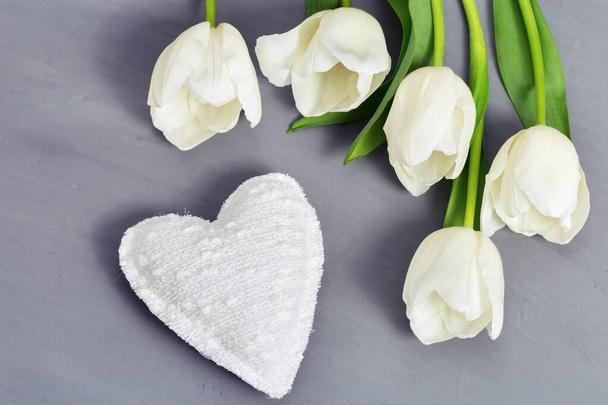 White tulip flowers and soft toy heart on gray concrete background with copy space. Greeting card for congratulations with love. Top view. - Fotografie, Obrázek