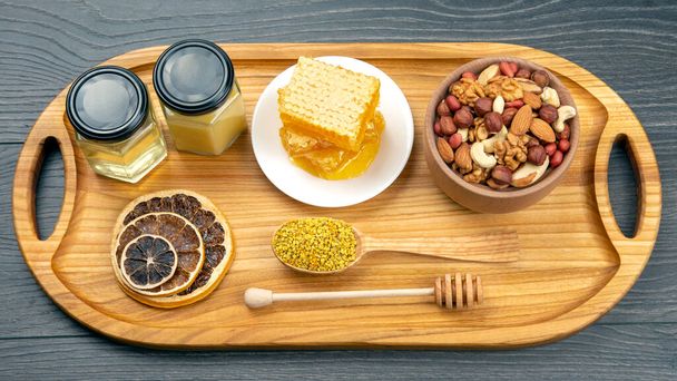 assortment of nuts and assorted dried citrus fruits and fresh floral honeycomb honey and pollen on kitchen wooden board. useful vitamin food for the human body - 写真・画像