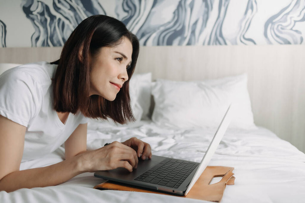 Woman works with laptop on the bed in concept of workation. - Fotoğraf, Görsel