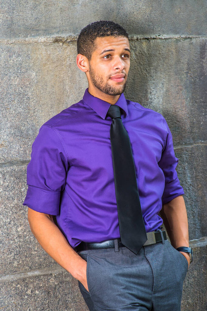 紫色のシャツにグレーのパンツと黒のネクタイを着た若い大学生が壁にもたれかかって外で考えています - 写真・画像