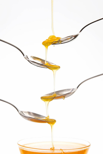 Il miele di fiore fresco gocciola da un cucchiaio in un cucchiaio su uno sfondo bianco. Alimenti vitaminici biologici. - Foto, immagini