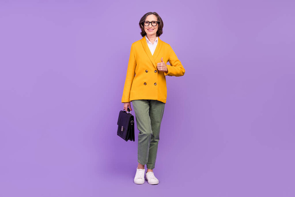 Full size photo of cheerful positive old lady make thumb-up hold suitcase business isolated on purple color background - Foto, immagini