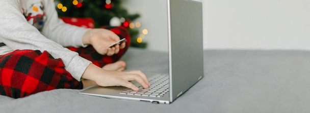 Рождественские покупки онлайн, продажи во время зимних каникул. Девушка держит карту и использует ноутбук. Длинный баннер для веб-страницы, дизайн с пространством для копирования, место для текста - Фото, изображение