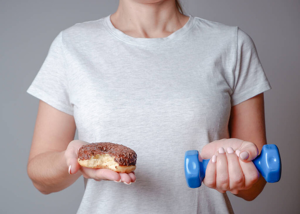 Dieet. Een vrouw die Donut en Dumbbell vasthoudt. Sweets zijn ongezond Junk Food. - Foto, afbeelding