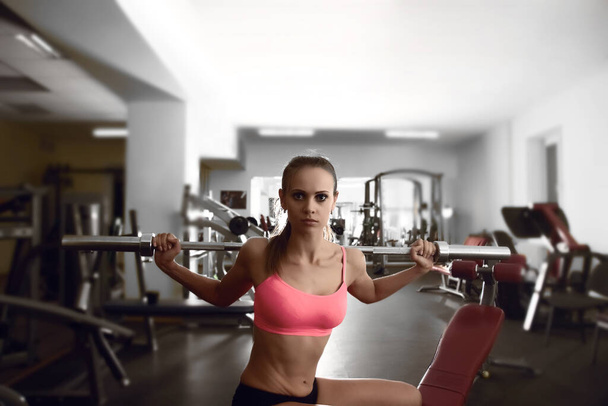 Determined woman working out with barbell bar while sitting on bench  in gym - Foto, Imagen