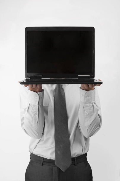 Unrecognizable business man holding his laptop with white blank screen at face height while standing on gray background.  businessman hides his face behind computer showing copy space. Banner Advertising - Φωτογραφία, εικόνα
