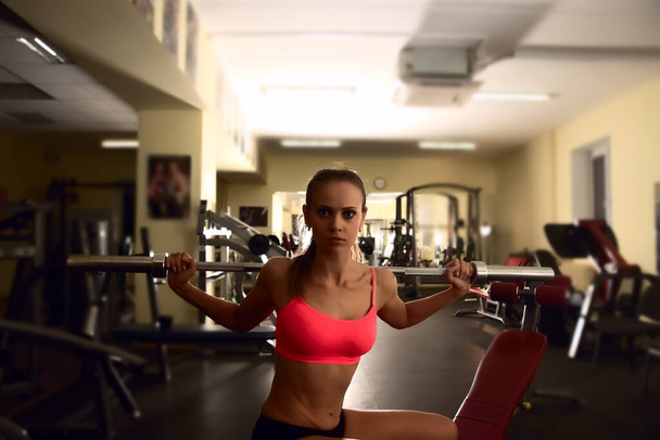 Determined woman working out with barbell bar while sitting on bench  in gym - Foto, Imagen