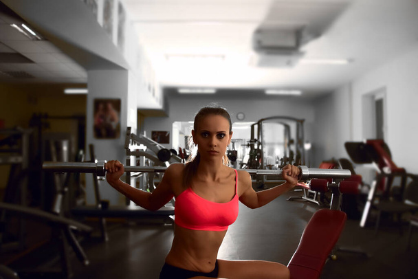 Determined woman working out with barbell bar while sitting on bench  in gym - Foto, afbeelding