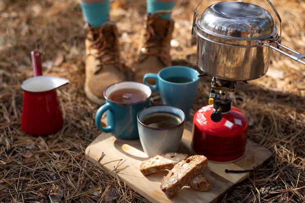 tourist picnic in the forest. burner with cauldron, cups and biscotti. camping aesthetic - Фото, изображение