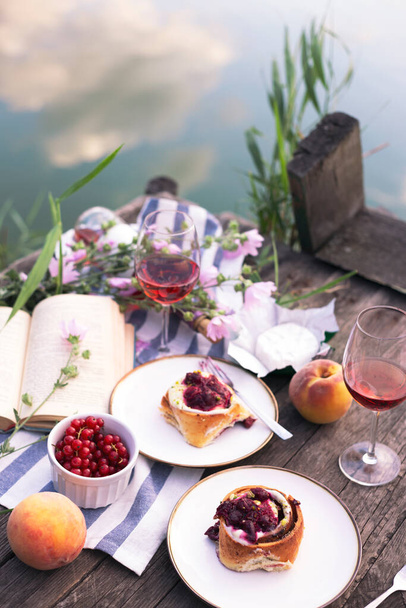 Summer still life-   picnic on a wooden pier. wine, sinabones, peaches, a book with a lake vie - Photo, image