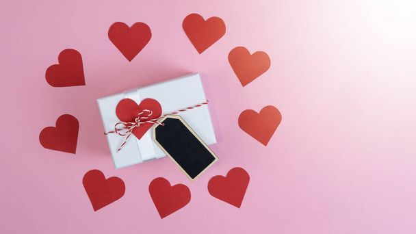 バレンタインデーの愛の結婚式のグリーティングカードテンプレート-ピンクの背景のテクスチャ上のビューに隔離された赤いハートと赤い白いリボンと白いギフトボックス/プレゼント、フラットレイ - 写真・画像