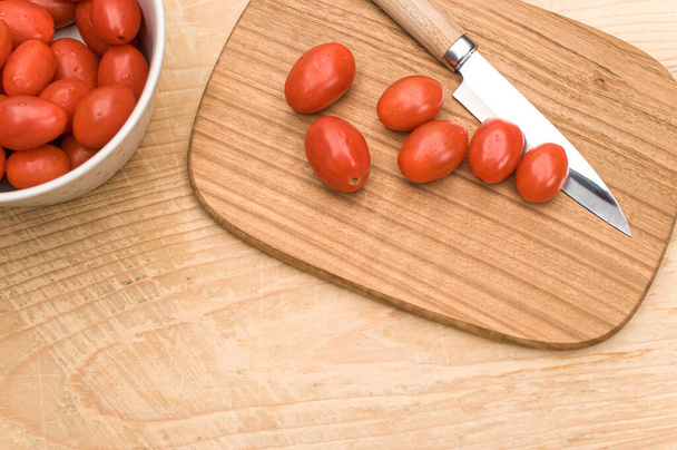 tigela cheia de tomates datterini com tábua de corte e faca em uma superfície de madeira com espaço de texto - Foto, Imagem