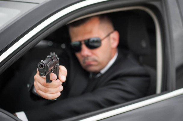 Police tactical car shooting training. Male spy agent bodyguard shooting from limousine. Security police in civilian black suit in action - Zdjęcie, obraz