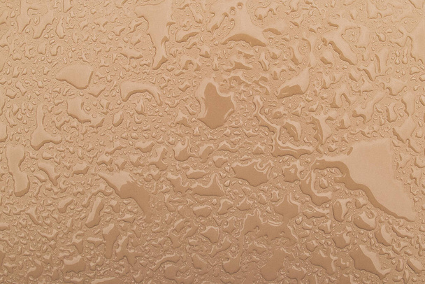 Irregular patterned water drops on a beige, sand-coloured shiny metal surface - Foto, Imagem