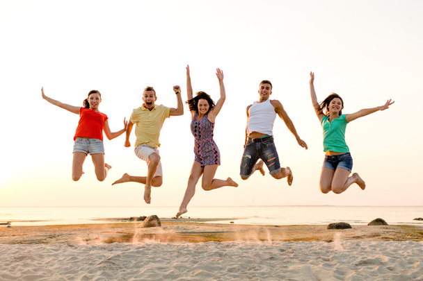 smiling friends dancing and jumping on beach - Photo, Image