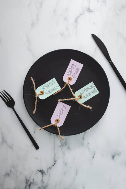 plant-based and animal-based labels next to dairy and dairy-free ones on top of black dining plate on marble table, concept of healthy nutrition and ethical choices - Фото, зображення