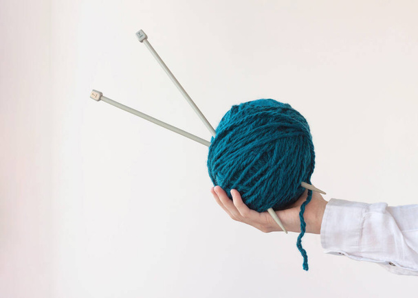 One hand holds a large ball of yarn and knitting needles. - Foto, Imagen