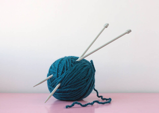 Large knitting needles are stuck in a large ball of blue yarn. - Φωτογραφία, εικόνα