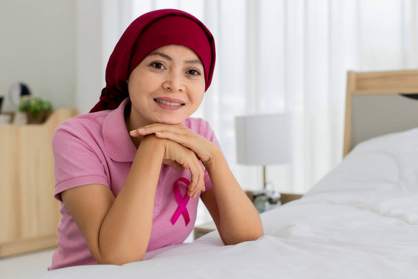Délicieuse femme asiatique sur chemise rose et couvrir la tête par écharpe rouge comme patiente du cancer du sein à l'hôpital souriant avec confiance et encourager le visage. - Photo, image