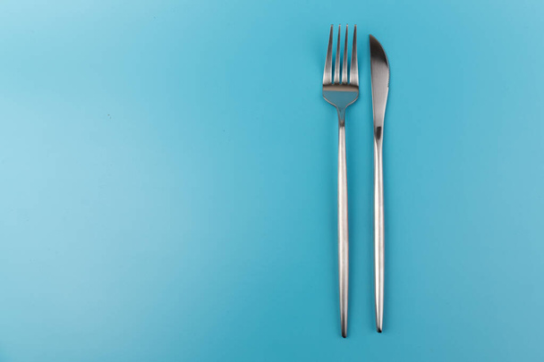 Un tenedor y un cuchillo sobre fondo azul. Plato plano Platos para desayuno, almuerzo o cena. Vista superior. Utensil de cocina. - Foto, Imagen