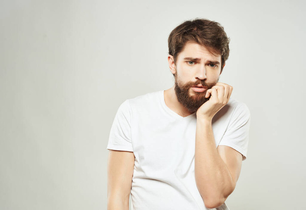 бородатый мужчина в белой футболке с раздраженным выражением лица в Студии. Высокое качество фото - Фото, изображение