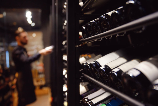 Şarap şişesi olan barmen şarap dükkanının yanında nefis içkilerle bekliyor. - Fotoğraf, Görsel
