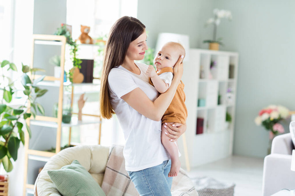 Photo of cute adorable mother dressed white t-shirt holding hands arms child smiling inside indoors apartment room - Foto, afbeelding